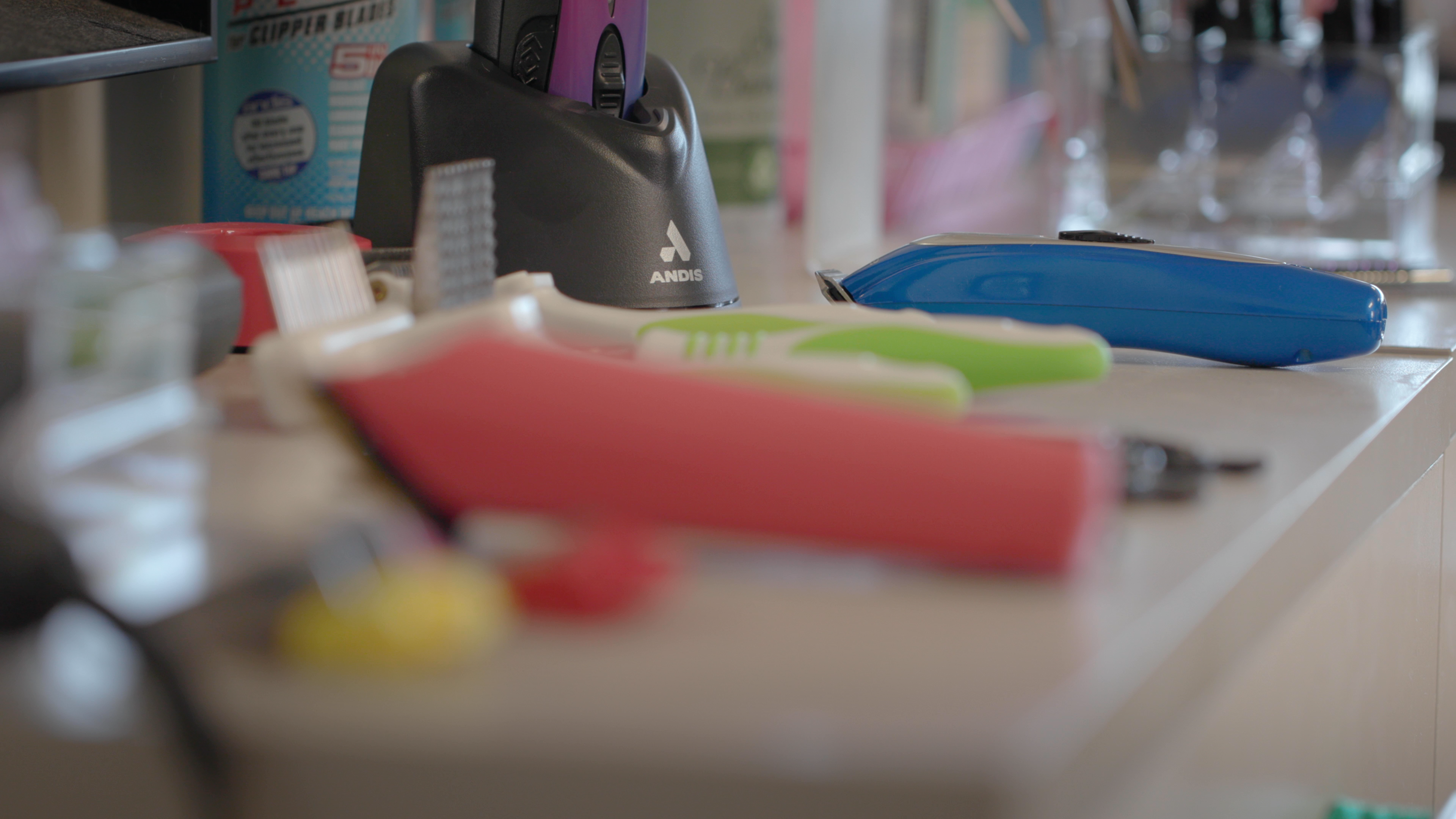 out of focus grooming tools in the foreground and charging dock with Andis logo in focus in the background