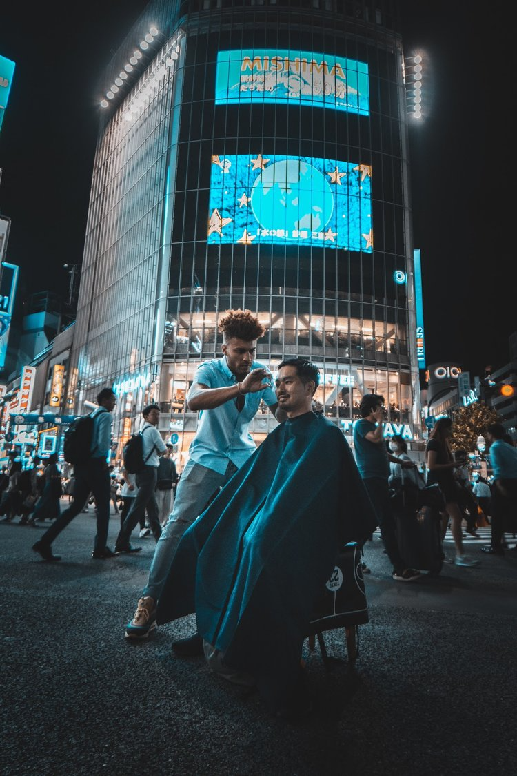 Julien Howard a.k.a. Velo Barber cutting a person's hair in the middle of an urban downtown street