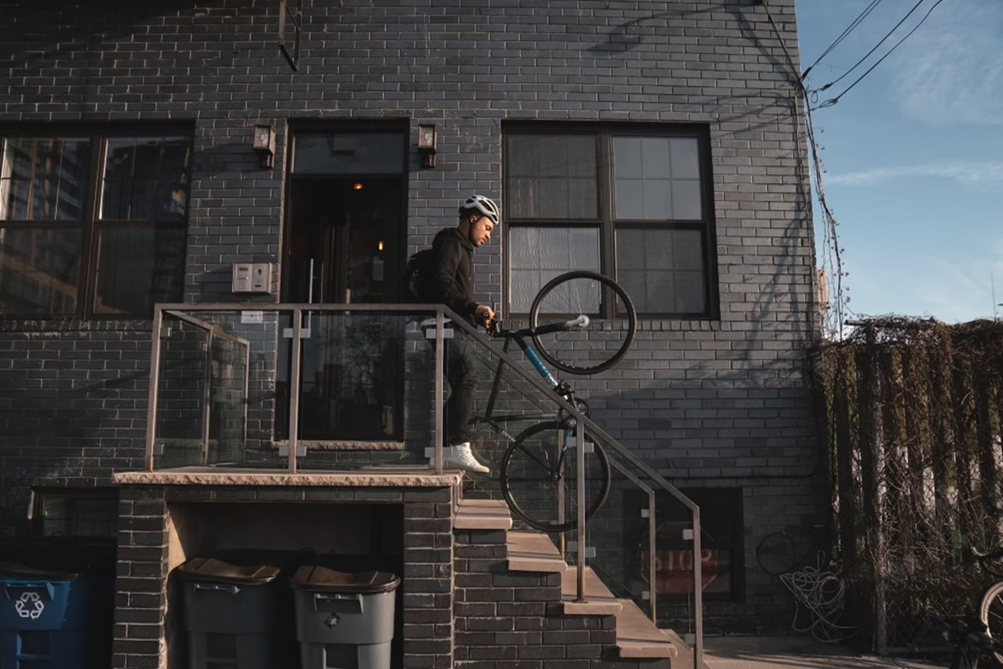 Julien Howard a.k.a. Velo Barber carrying a bicycle down a set of stairs on a porch landing